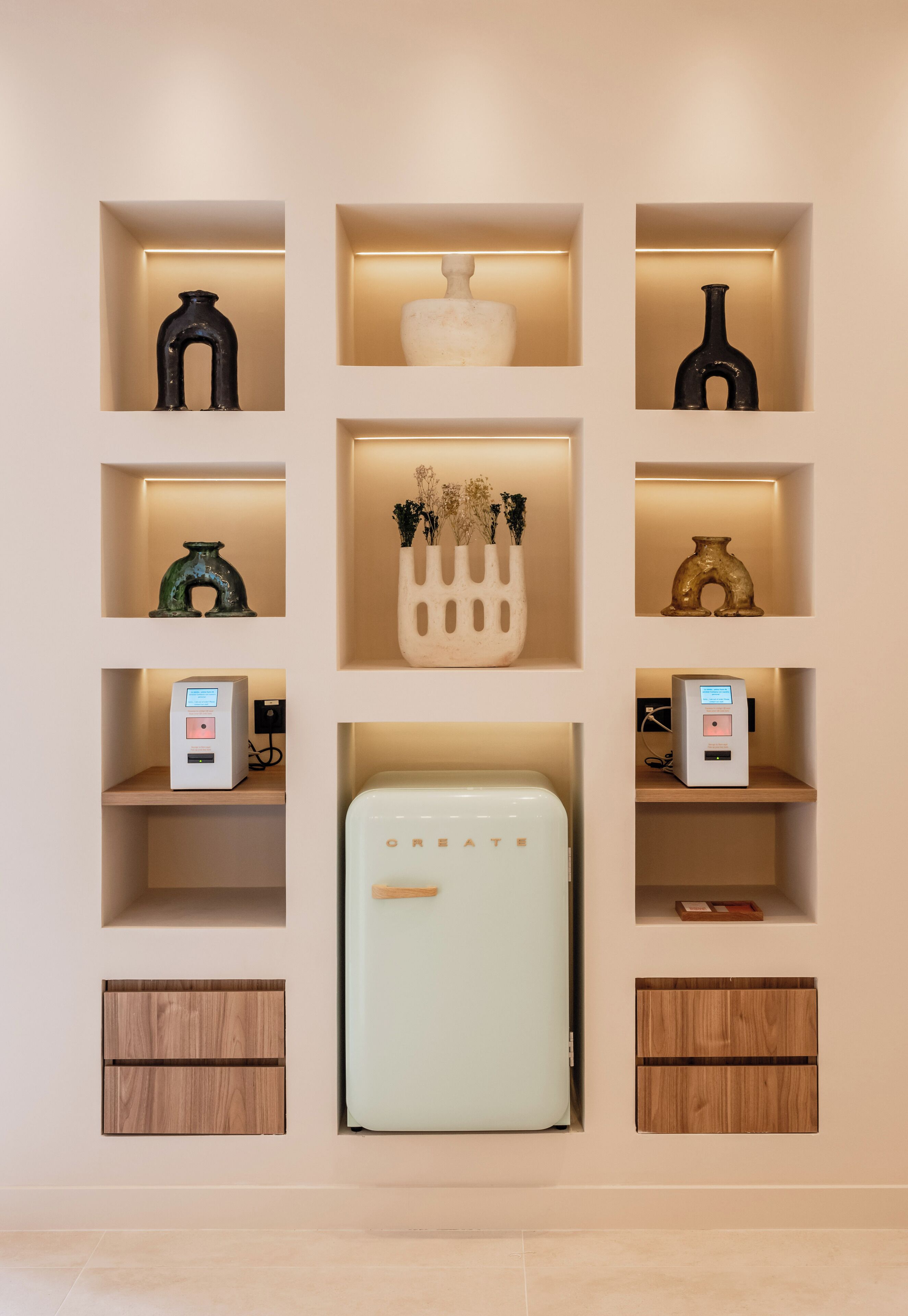 A wall with multiple shelves containing various items such as vases, a refrigerator, and a small electronic device.