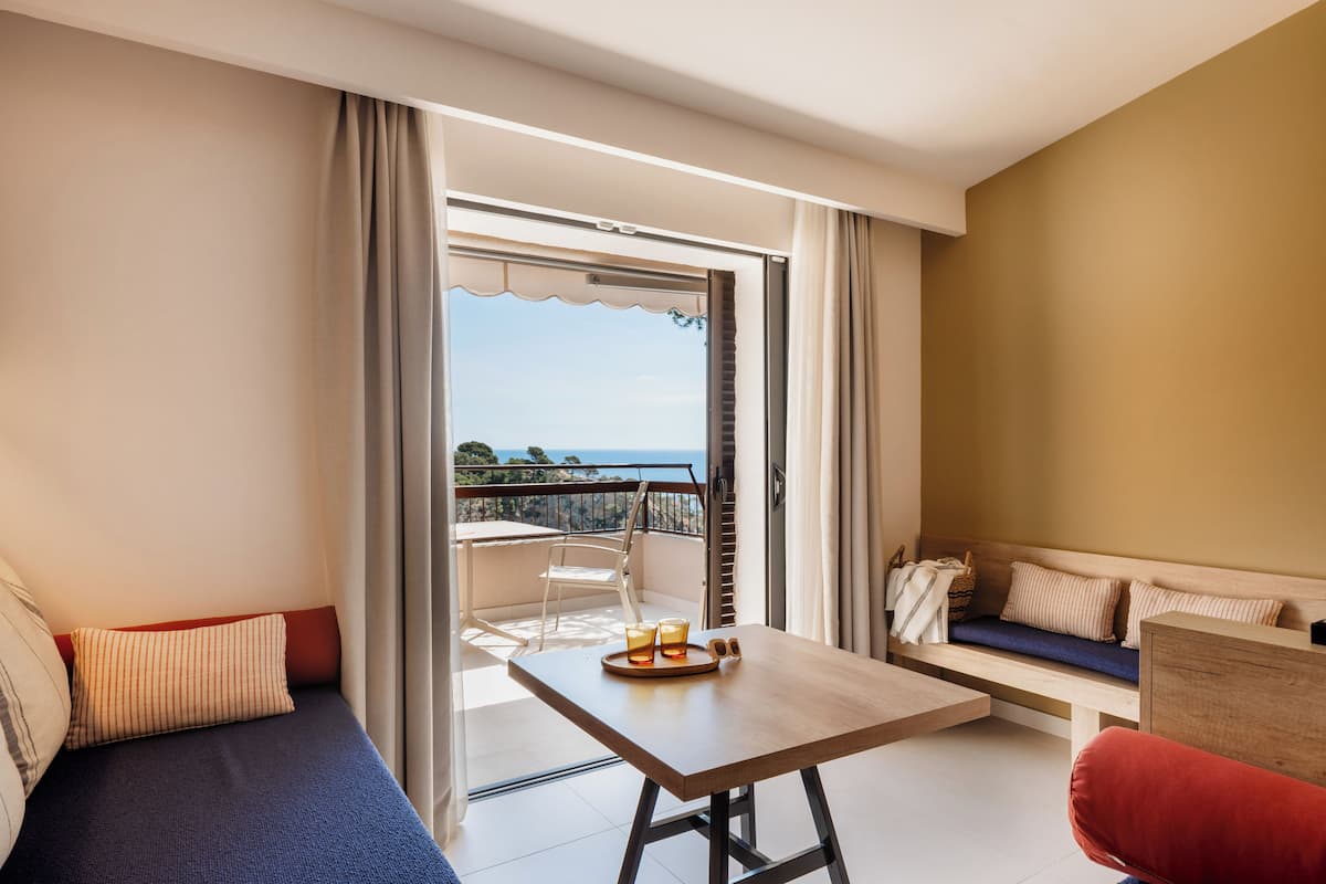 Ein modernes Hotelzimmer mit Balkon, einer Sitzecke, einem Esstisch und Meerblick.