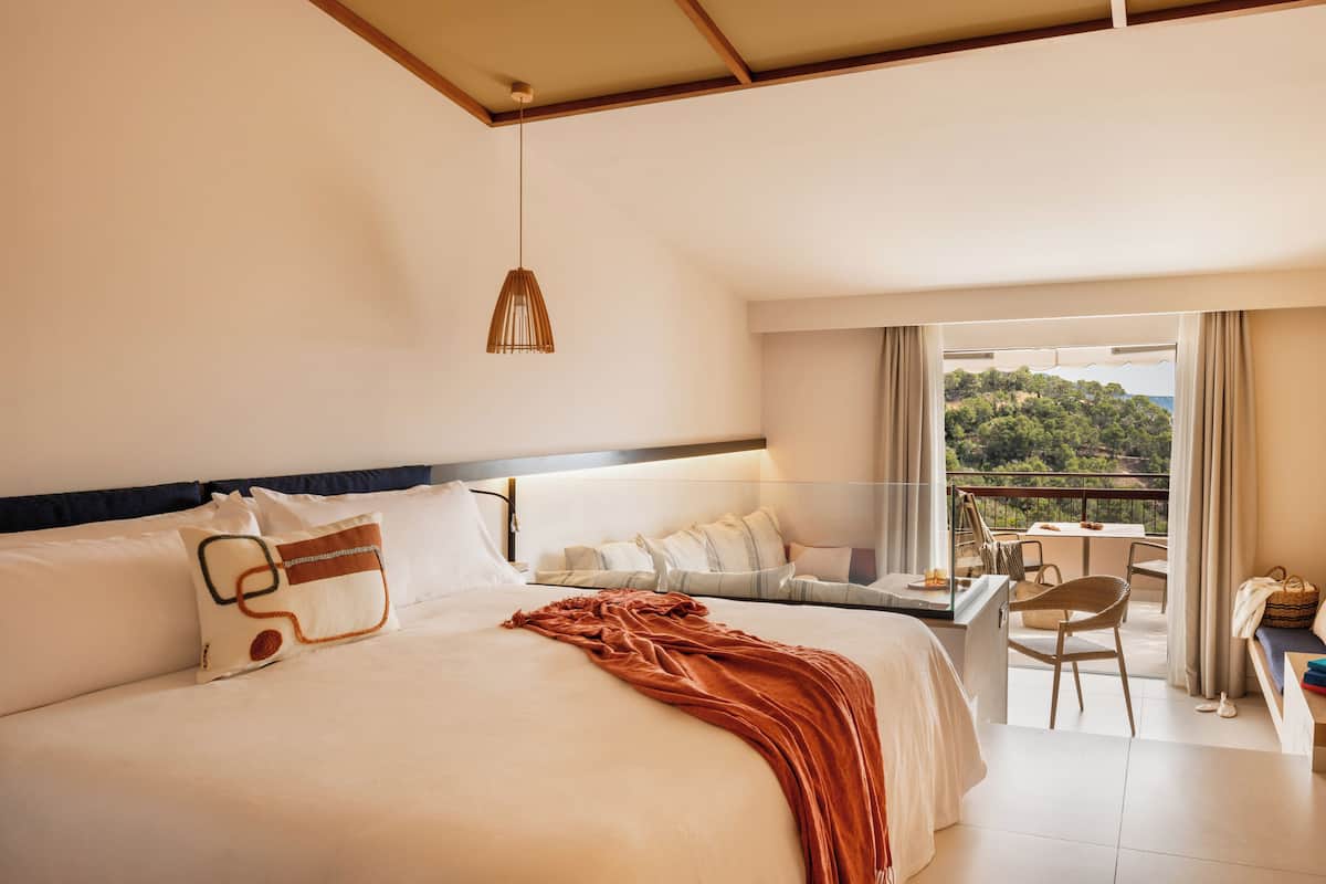 Ein Hotelzimmer mit einem großen Bett, einem Balkon mit Tisch und Stühlen sowie Blick auf Grünflächen.