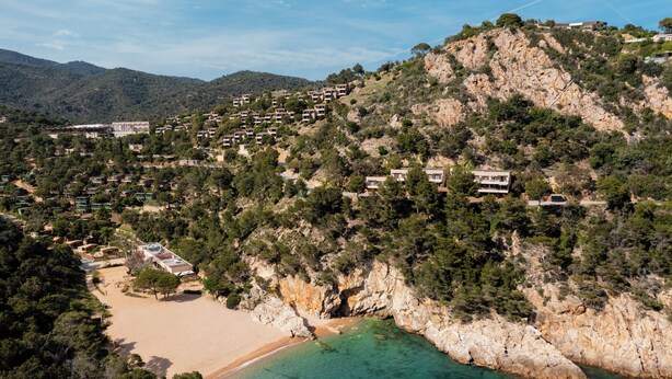 Un pueblo costero con casas escalonadas, una playa de arena y aguas turquesas cristalinas.