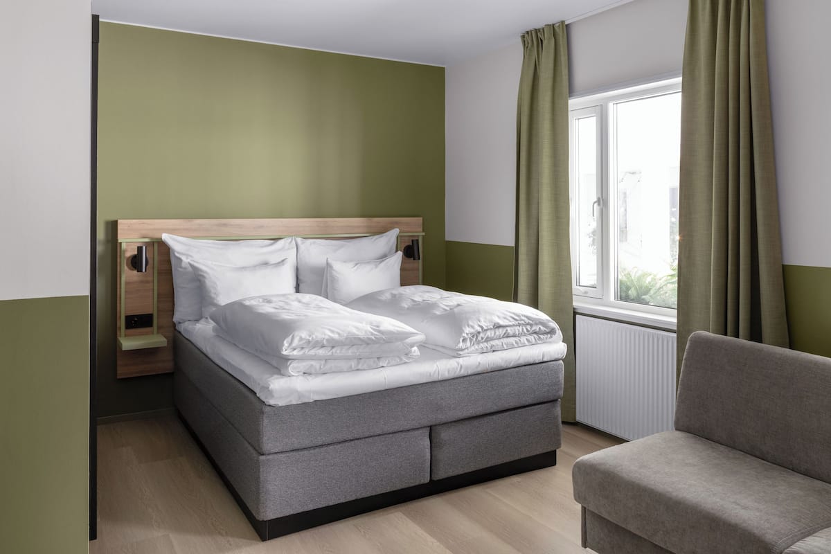 Un dormitorio ordenado con una cama, una mesita de noche, una silla y una ventana con cortinas.