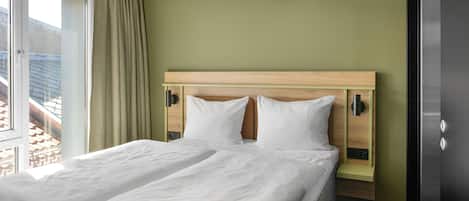 A neatly made bed in a room with a green wall and a window with curtains.