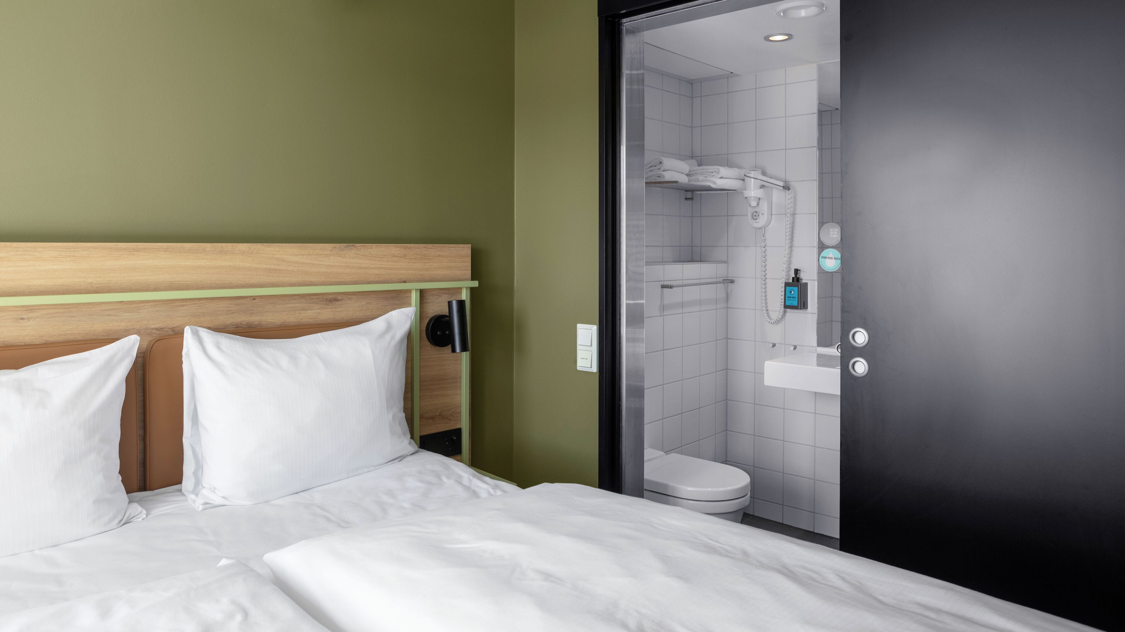 A hotel room with a wooden headboard, white bedding, a toilet, and a shower area.
