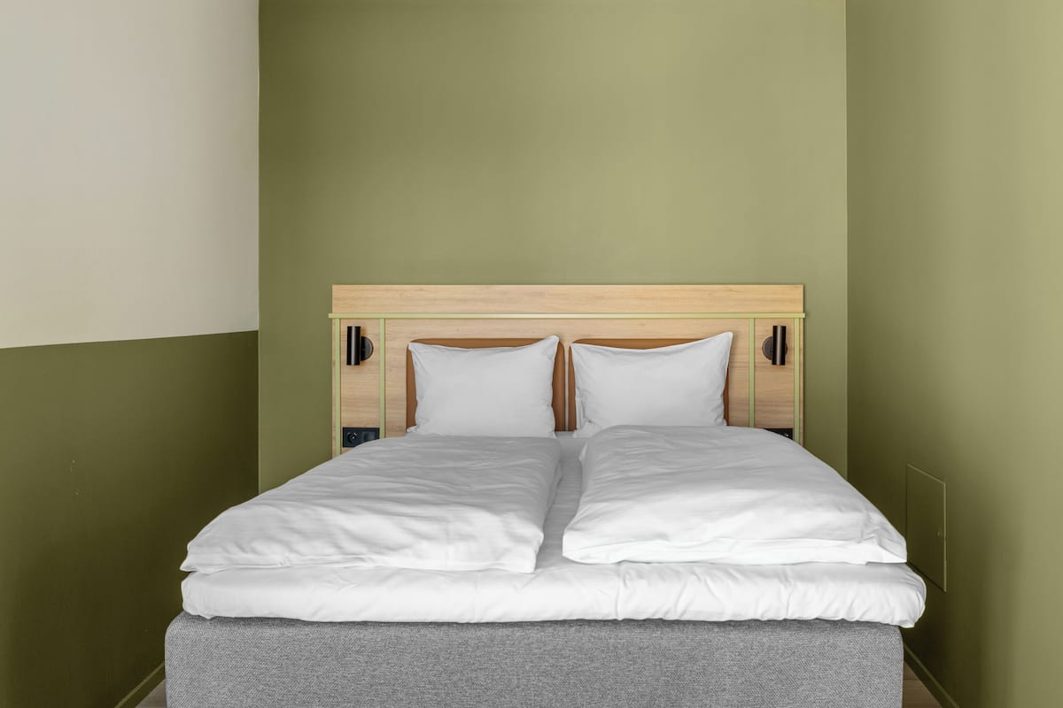 Una cama bien hecha con sábanas blancas en una habitación con paredes verdes y un cabecero de madera.