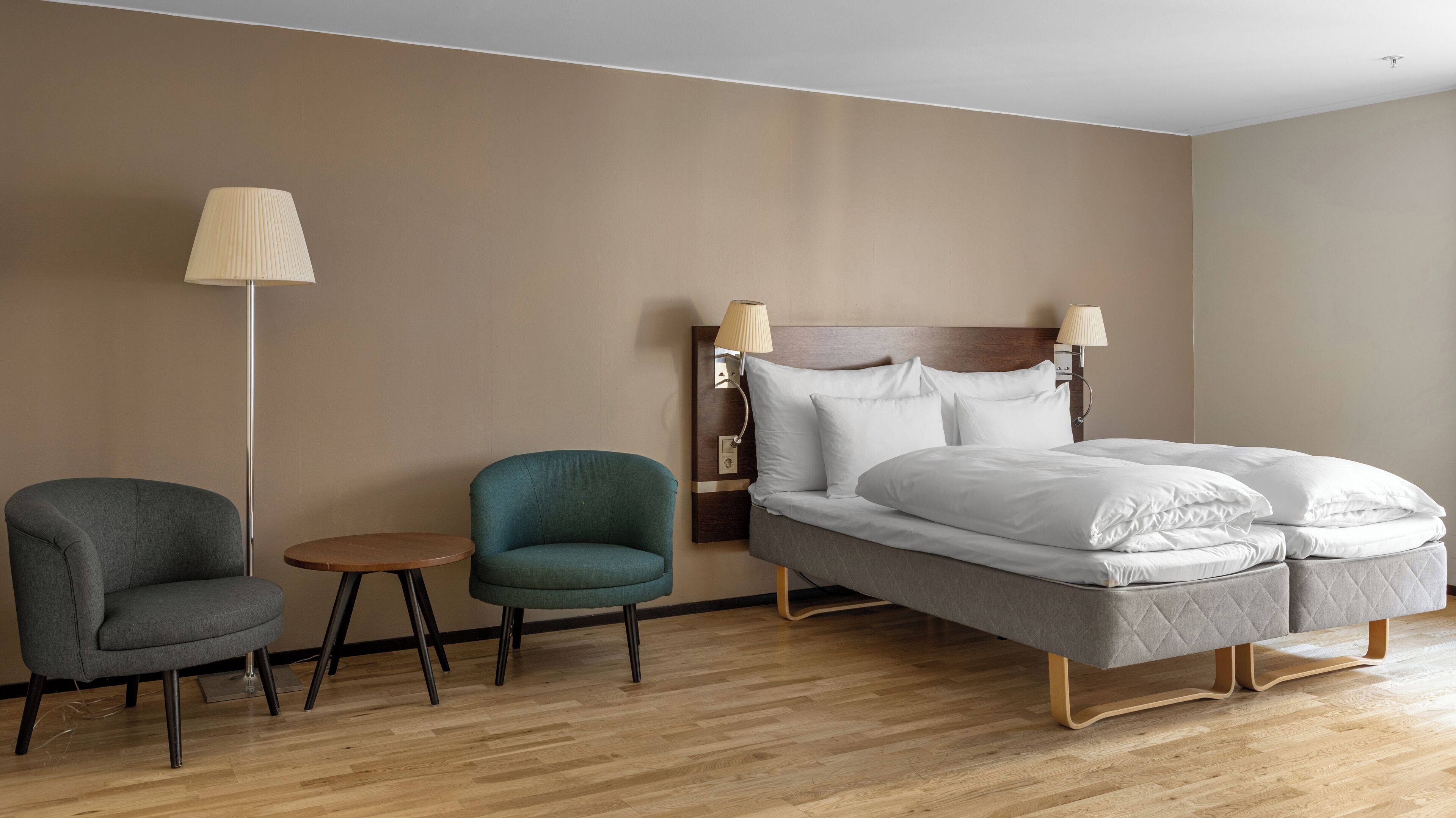 A hotel room with a bed, two armchairs, a small round table, and two wall-mounted lamps.