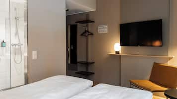 A hotel room with a bed, a TV, a shower, and a small table.