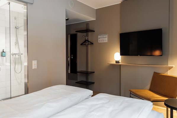 A hotel room with a bed, a TV, a shower, and a small table.