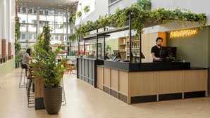 Un área de bar moderna con un letrero de neón, mostrador de madera y plantas en macetas.