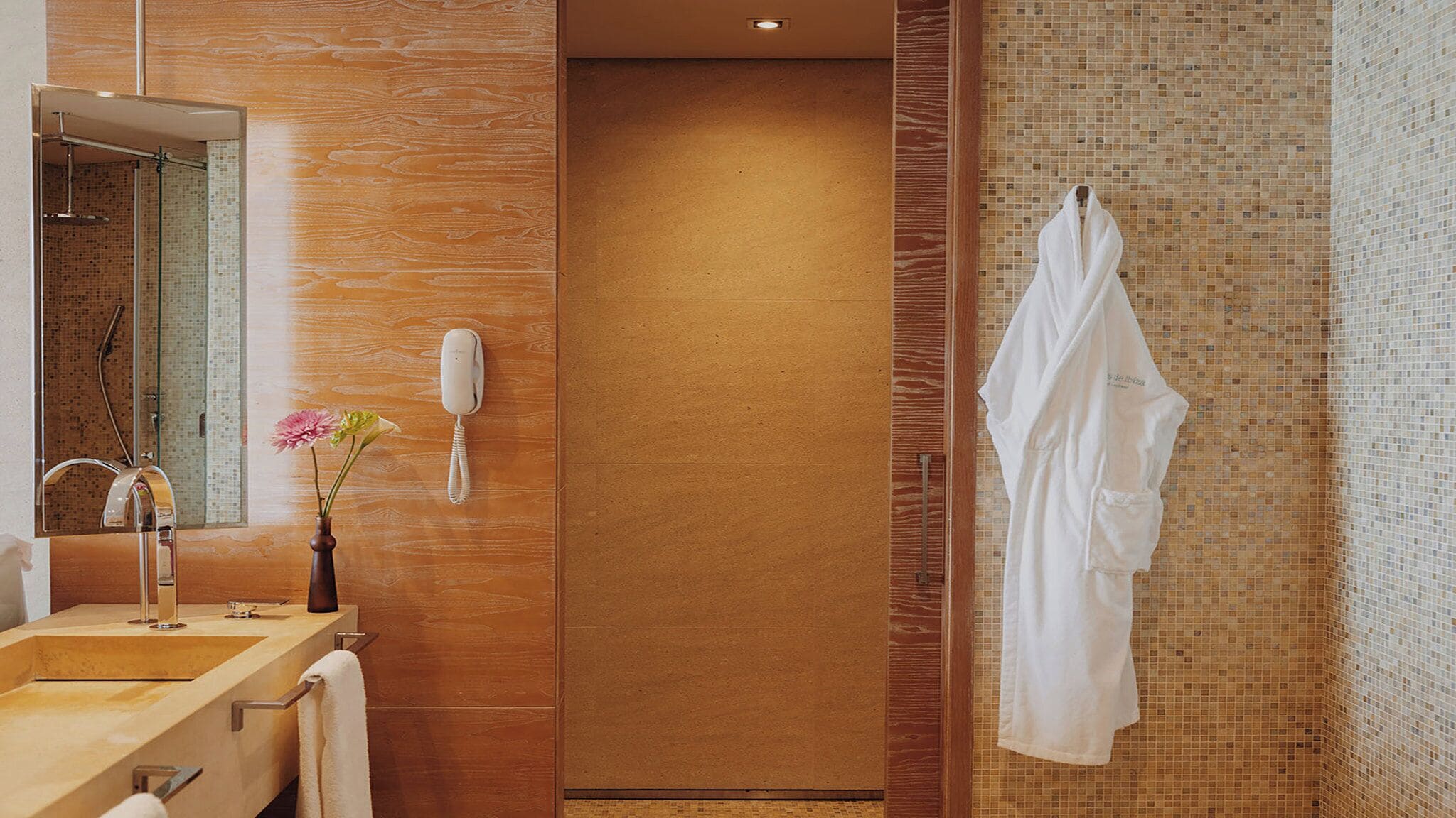 Un baño moderno con un mueble de tocador de madera, un espejo, un teléfono y un perchero para toallas.