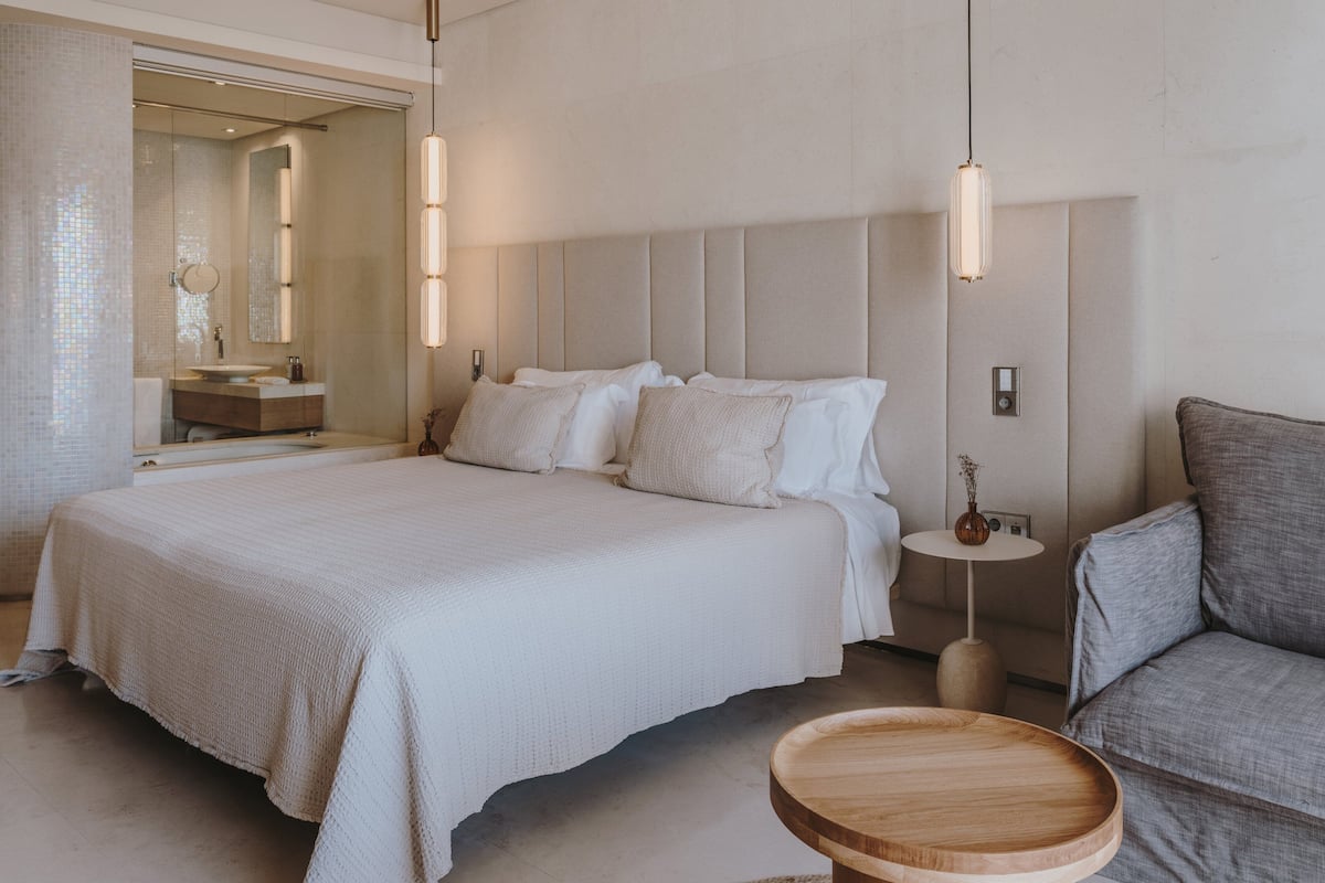 Une chambre à coucher moderne avec un grand lit, des tables de chevet, une petite table d’appoint ronde en bois et un canapé.