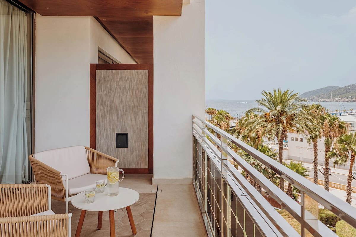 Un balcon agrémenté de meubles en osier, une petite table avec des boissons, et une vue sur la mer et les palmiers.