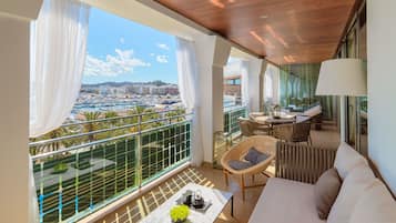 A balcony with a view of a marina and buildings, furnished with a sofa, chairs, and a table with a vase of flowers.