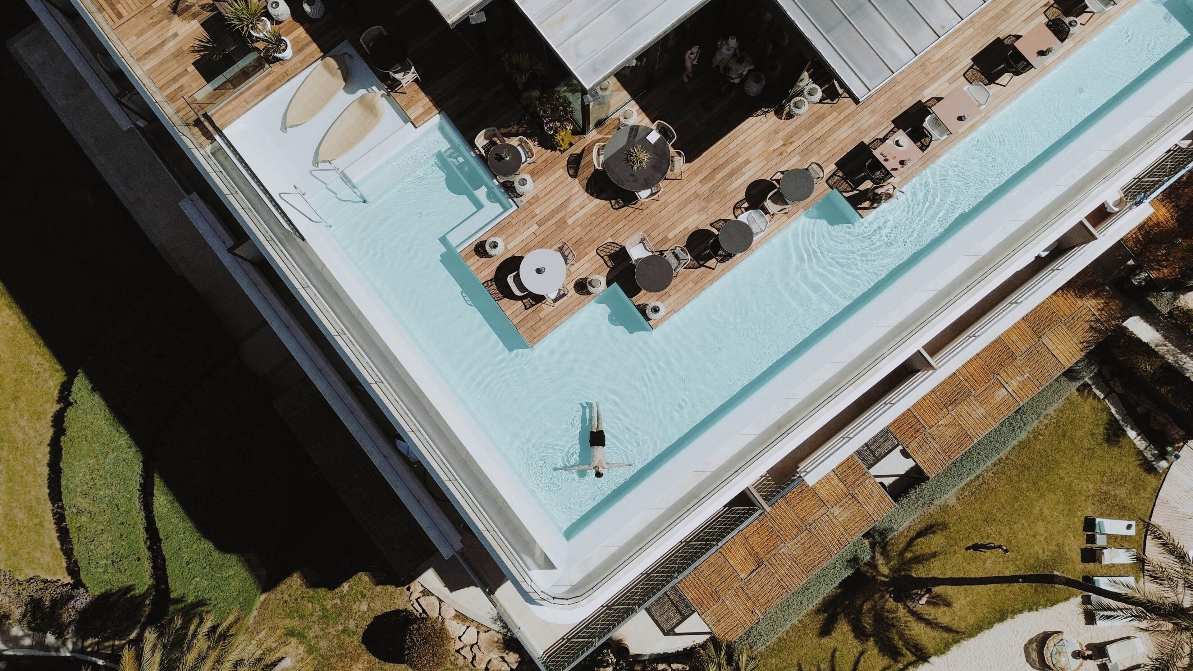 Vista aérea de un hotel con piscina, mobiliario exterior y un jardín bien cuidado.