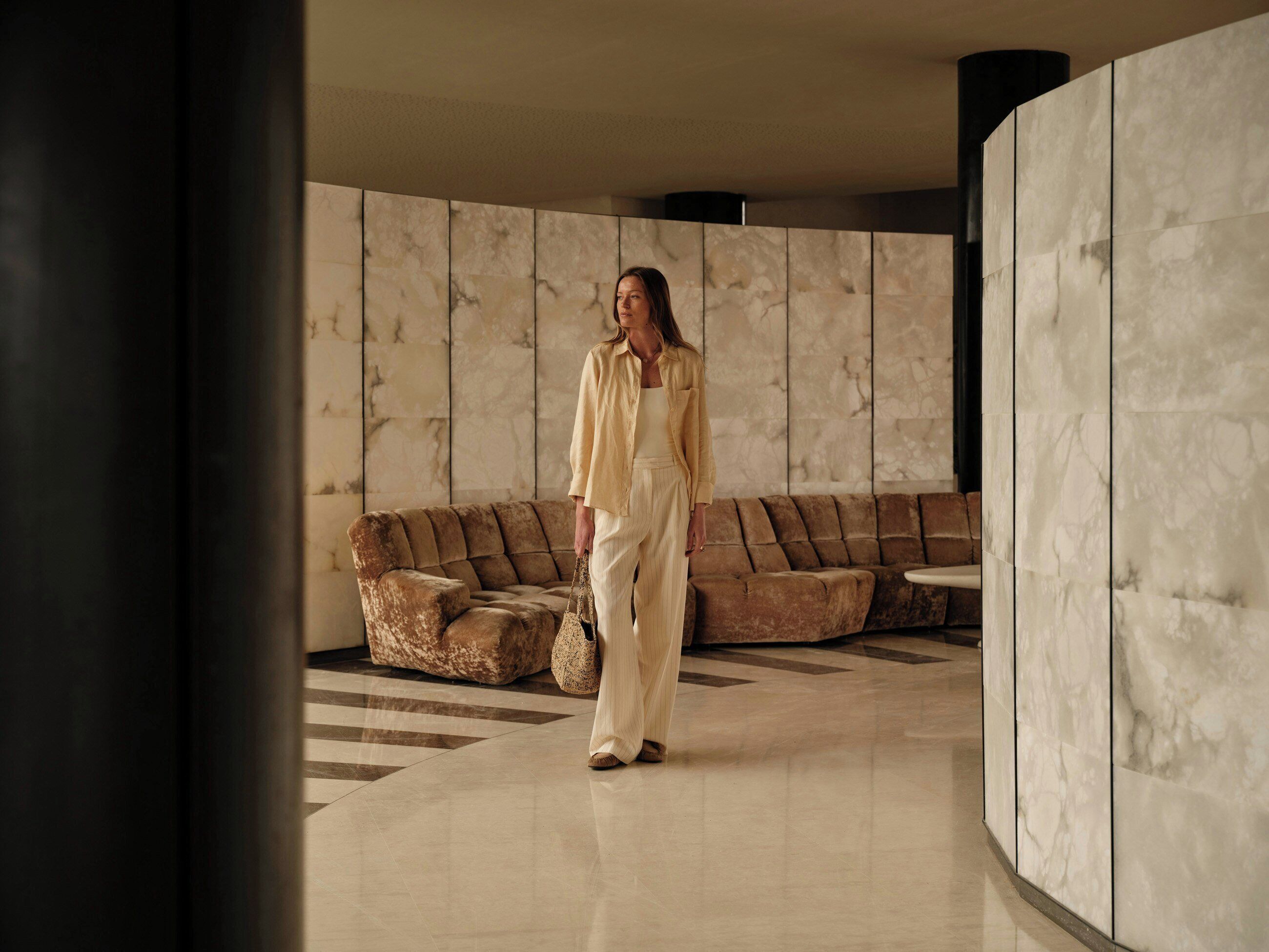 A person walking in a lobby with a marble wall and a brown sofa.