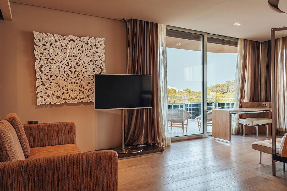 Une chambre d’hôtel moderne dotée d’une grande télévision à écran plat, d’un canapé, d’un bureau avec une chaise et d’un balcon offrant une vue agréable.