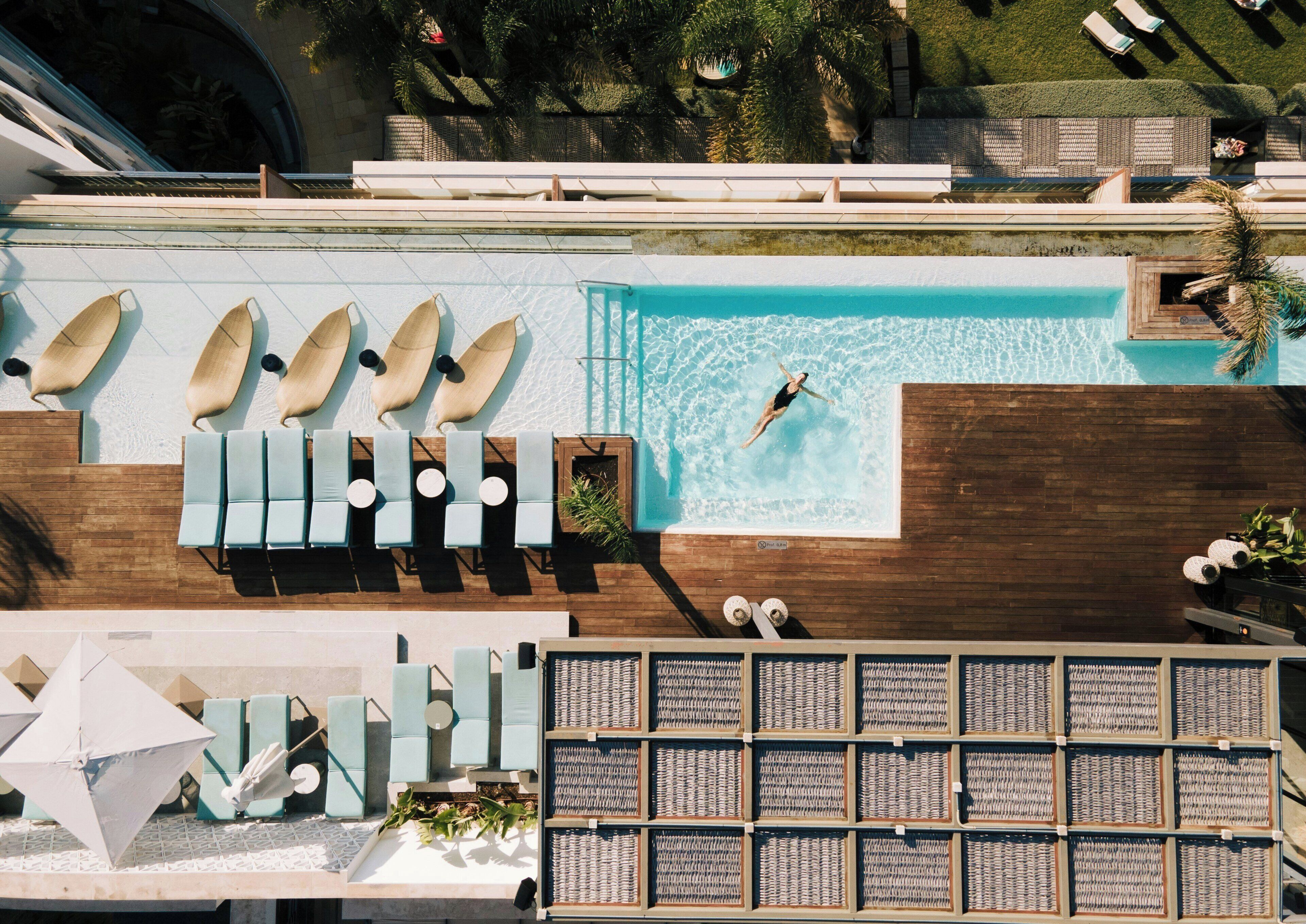 Vue aérienne d’un espace piscine comprenant des chaises longues, une piscine et une terrasse ensoleillée avec des parasols.