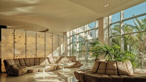 Een ruime lobby met een grote hoekbank, een potplant en grote ramen.