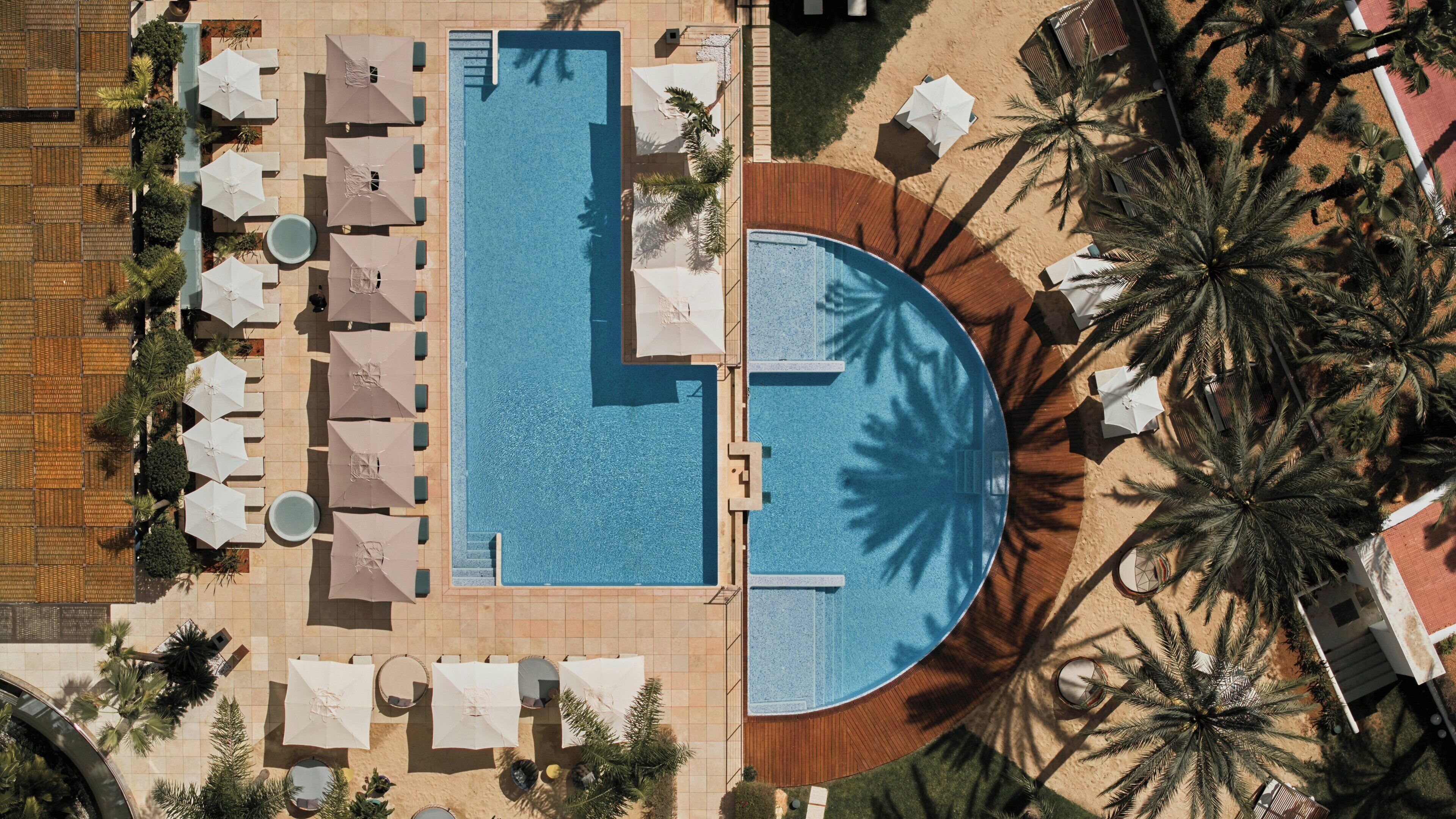 Vista aérea de um resort com uma piscina grande, espreguiçadeiras e palmeiras.