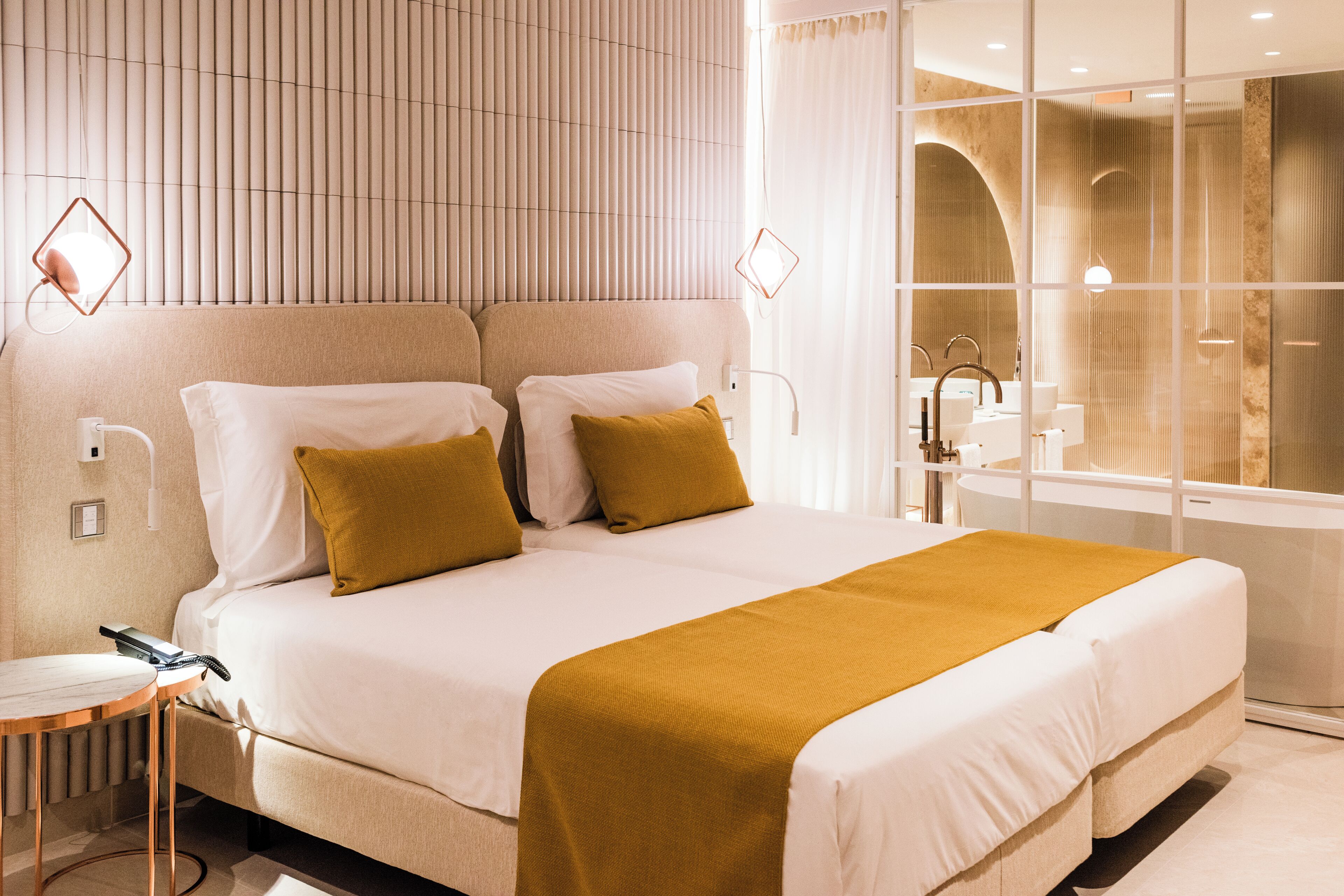 A modern hotel room with a large bed, bedside tables, a bathroom with a bathtub, and a window with curtains.
