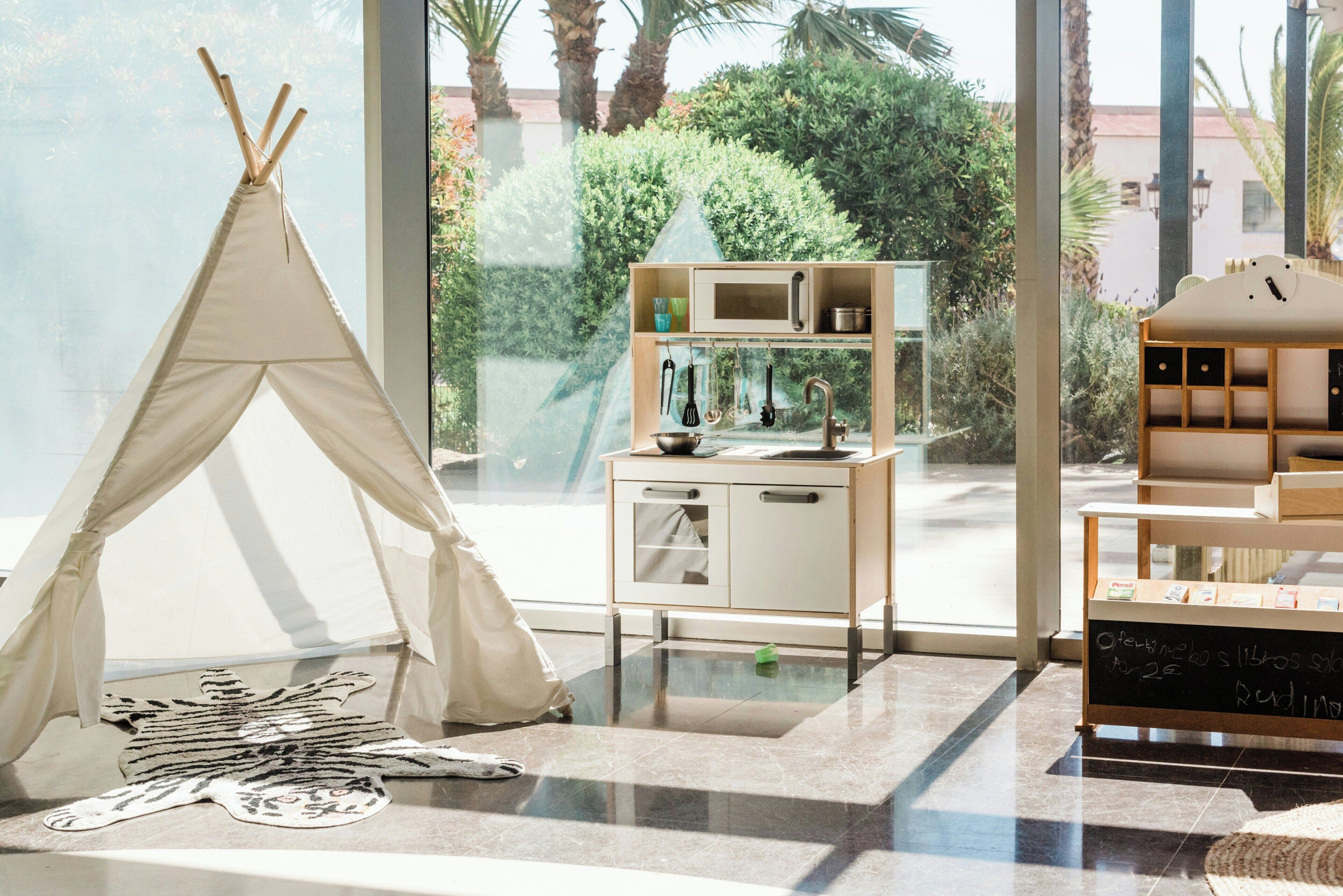 A room with a teepee, a kitchenette, and a view of greenery.