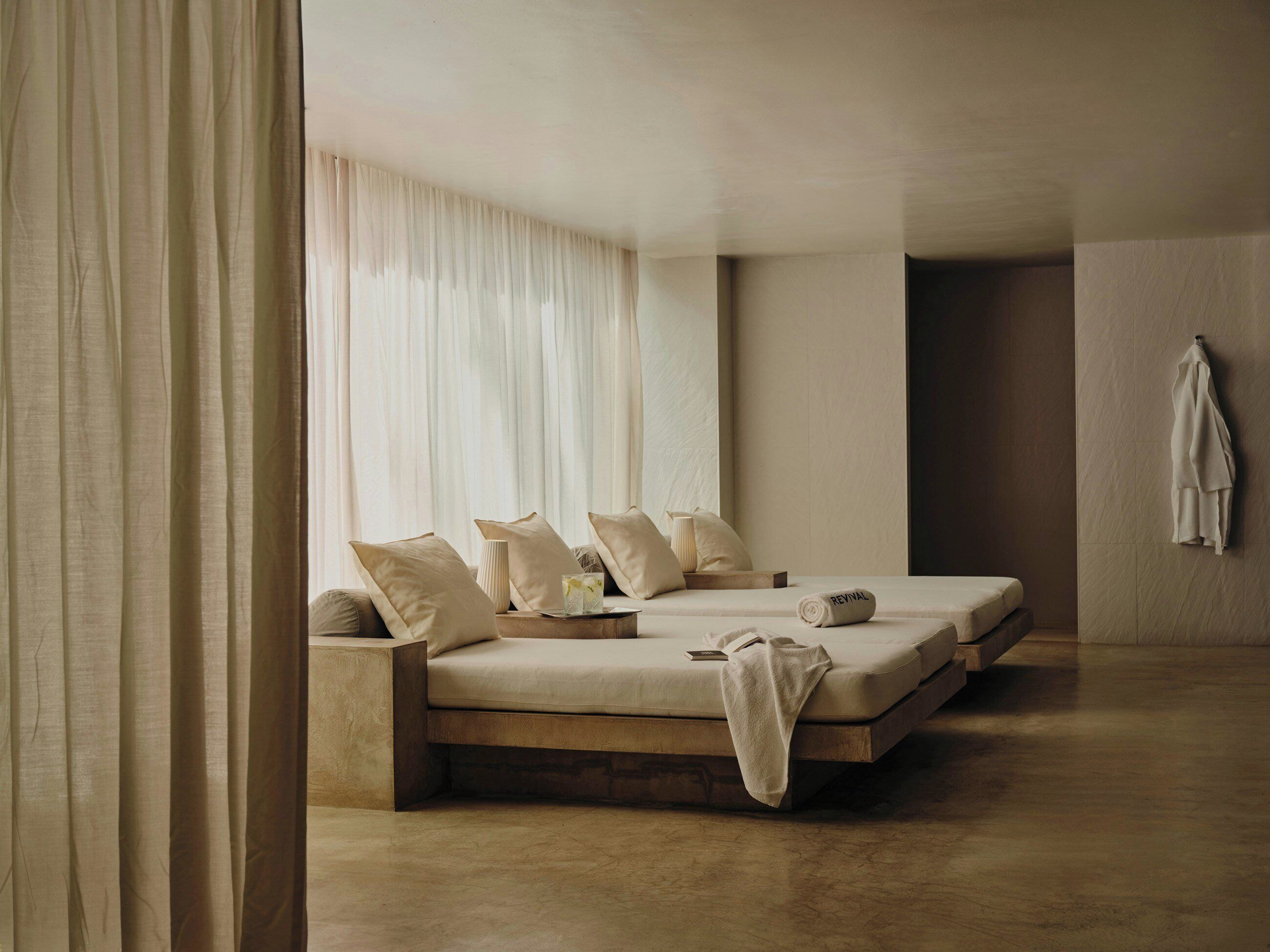 A minimalist bedroom with a large bed, a smaller bed, a bedside table, and a hanging towel.
