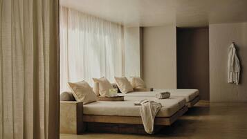 A minimalist bedroom with a large bed, a smaller bed, a bedside table, and a hanging towel.