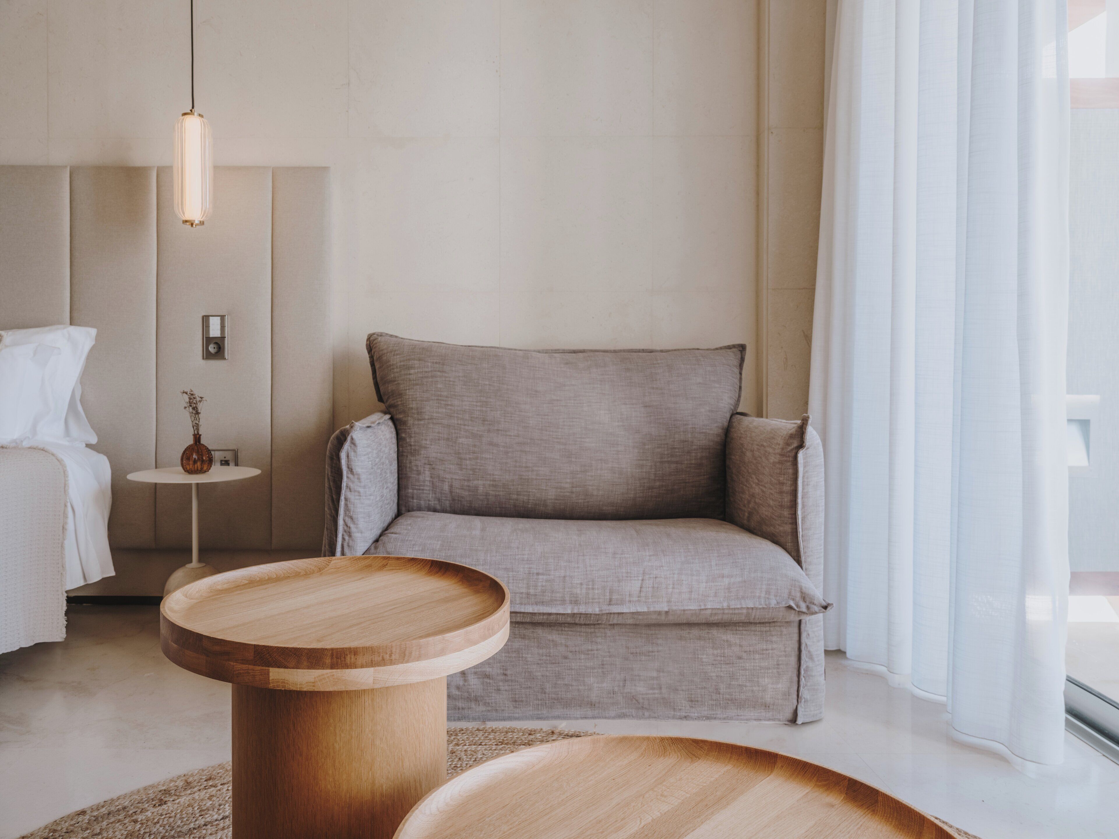 A modern, minimalist room with a sofa, a round wooden table, and a hanging light fixture.