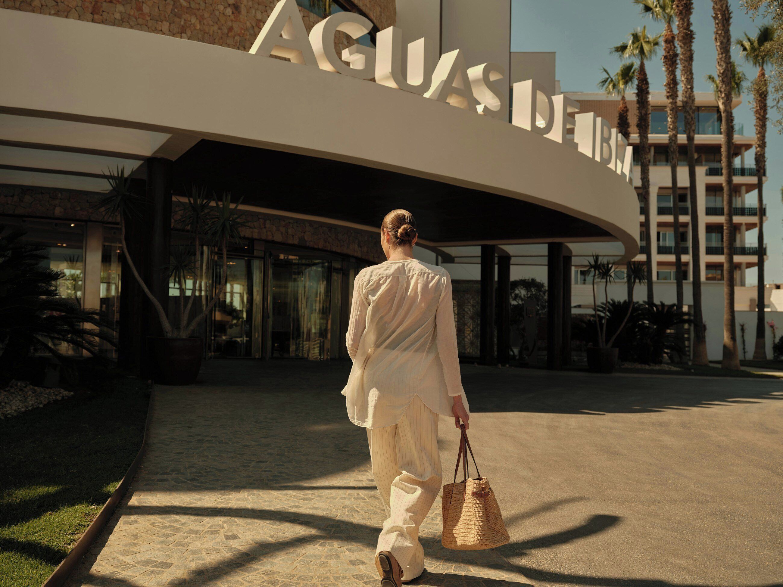 Eine Person geht auf ein Gebäude mit der Beschilderung 'AGUAS DELFIN' zu, was auf ein Hotel oder Resort hindeutet.
