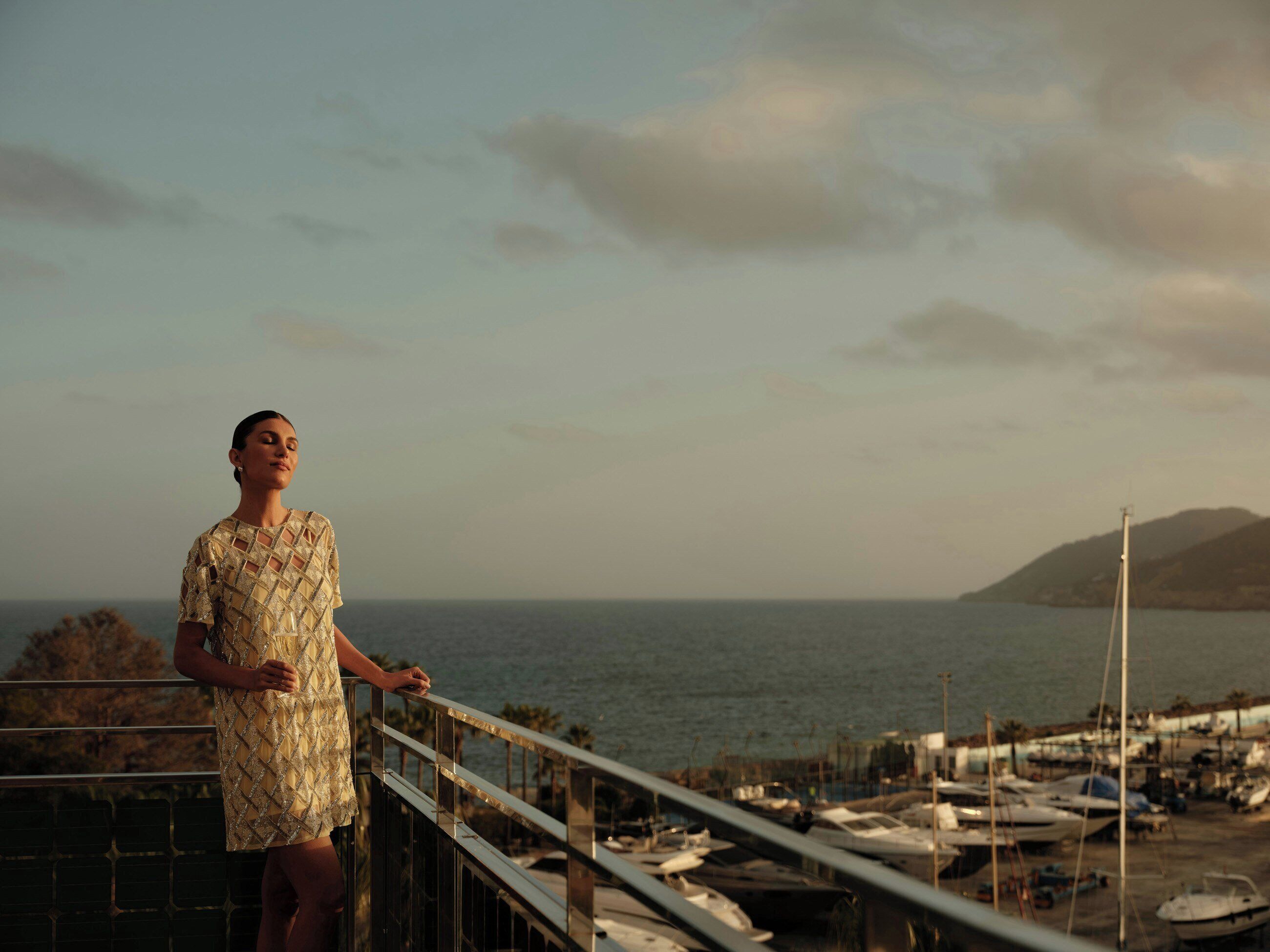 Eine Person steht auf einem Balkon mit Blick auf eine Marina, Boote und das Meer.