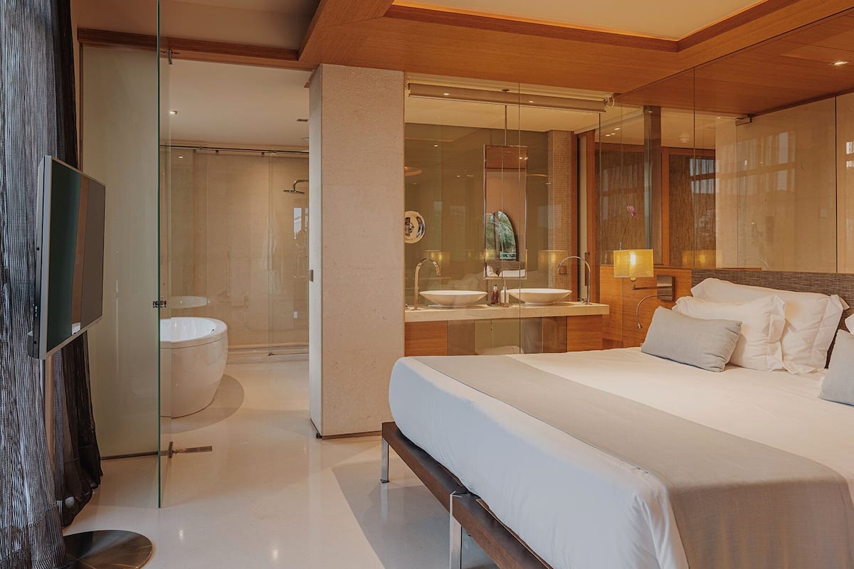Une chambre d’hôtel moderne dotée d’un grand lit, d’une douche à parois de verre, d’une coiffeuse avec un miroir et d’un téléviseur à écran plat.