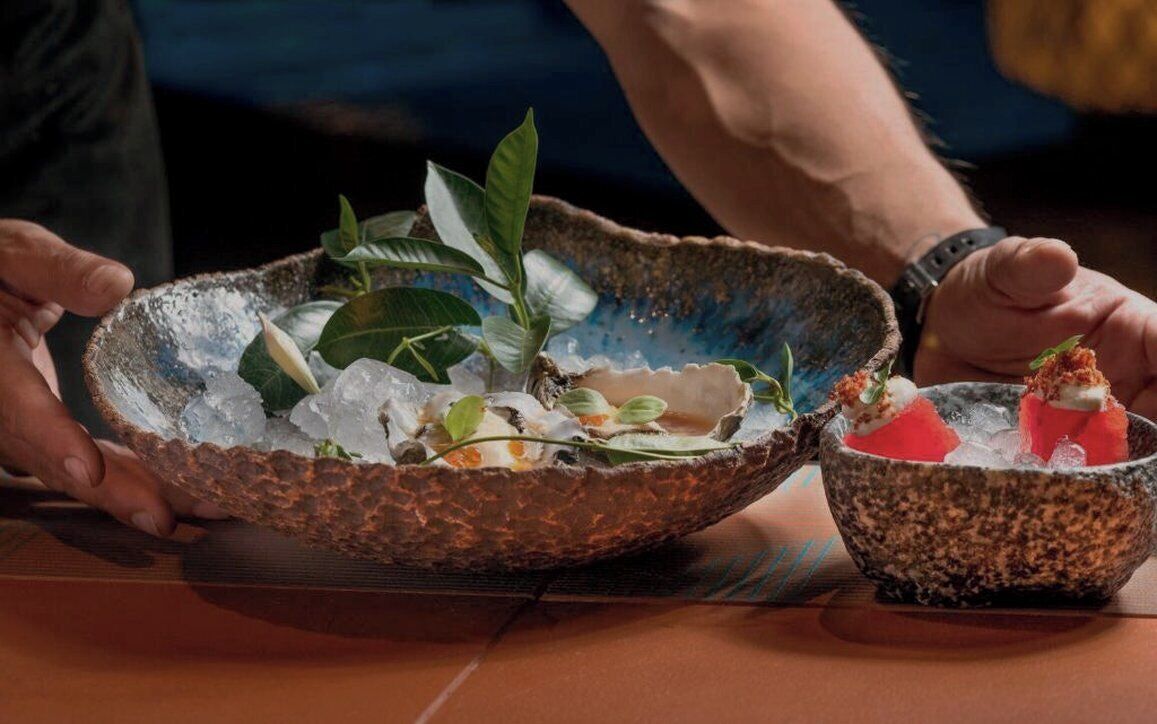 A person holding a bowl with ice and food items, and another bowl with a food item on a table.
