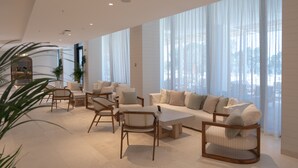 A modern living room with a sofa, chairs, and a coffee table. There are large windows with sheer curtains.
