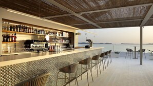 A bar area with a long counter, multiple shelves of bottles, and bar stools.