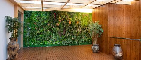 Una habitación con piso de madera, un jardín vertical verde y dos jarrones grandes.