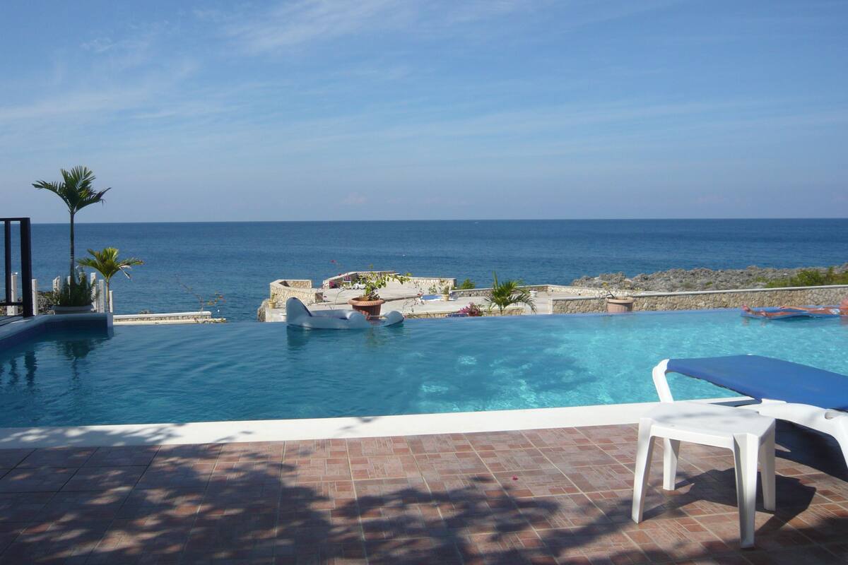 Une piscine avec vue sur la mer, un fauteuil de relaxation et une petite table.