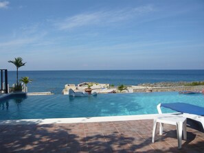 A swimming pool with a view of the sea, a lounge chair, and a small table. - Mirage Resort - Clothing Optional - Adults Only (Negril)