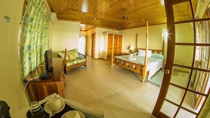 Een kamer met een houten plafond, een bed met hemel, een bank, een televisie en een eethoek met een tafel en stoelen.