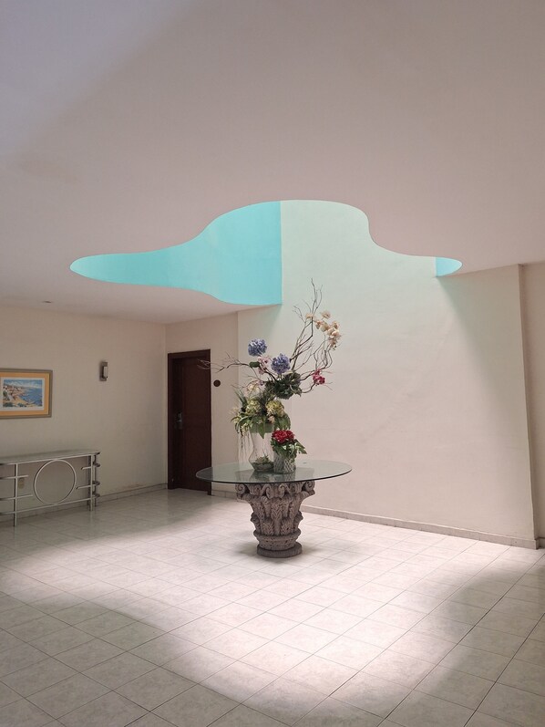 Un vestíbulo con una mesa redonda de cristal en el centro de un piso de baldosas, un cuadro en la pared y una puerta al fondo.