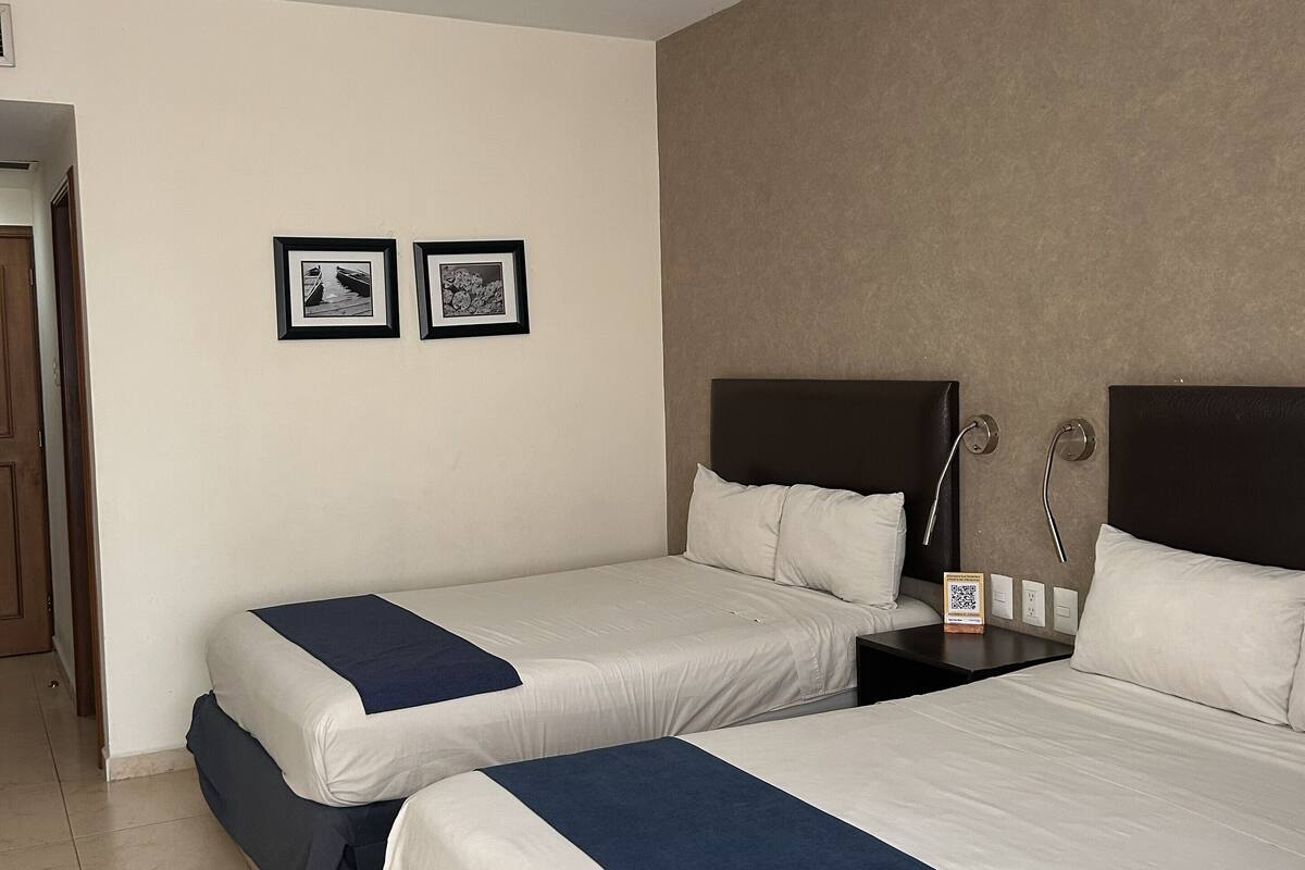 A hotel room with two beds, a door, and two framed pictures on the wall.