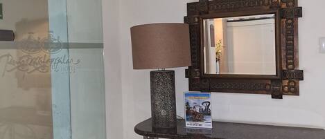 A hotel lobby with a glass door, a lamp, a mirror, and a small table.