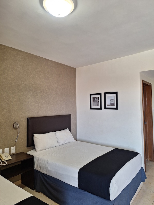 Una habitación de hotel con una cama, mesita de noche y un cuadro colgado en la pared.