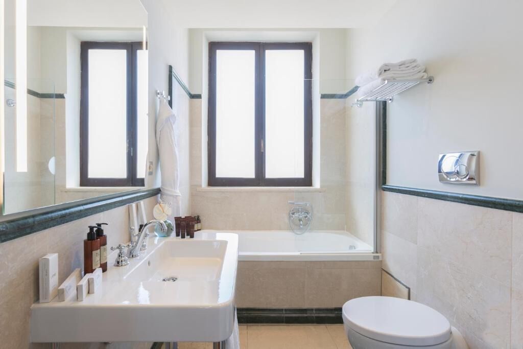 A bathroom with a sink, mirror, window, bathtub, and toilet.