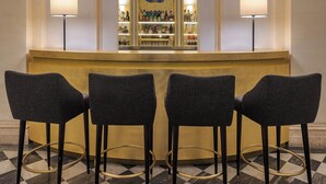 A bar area with three bar stools, a mirror above the bar, and a bar stocked with bottles. - Donna Camilla Savelli – VRetreats (Rome)
