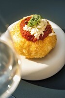 A round, yellow-colored food item with a red sauce and white topping, served on a white plate.