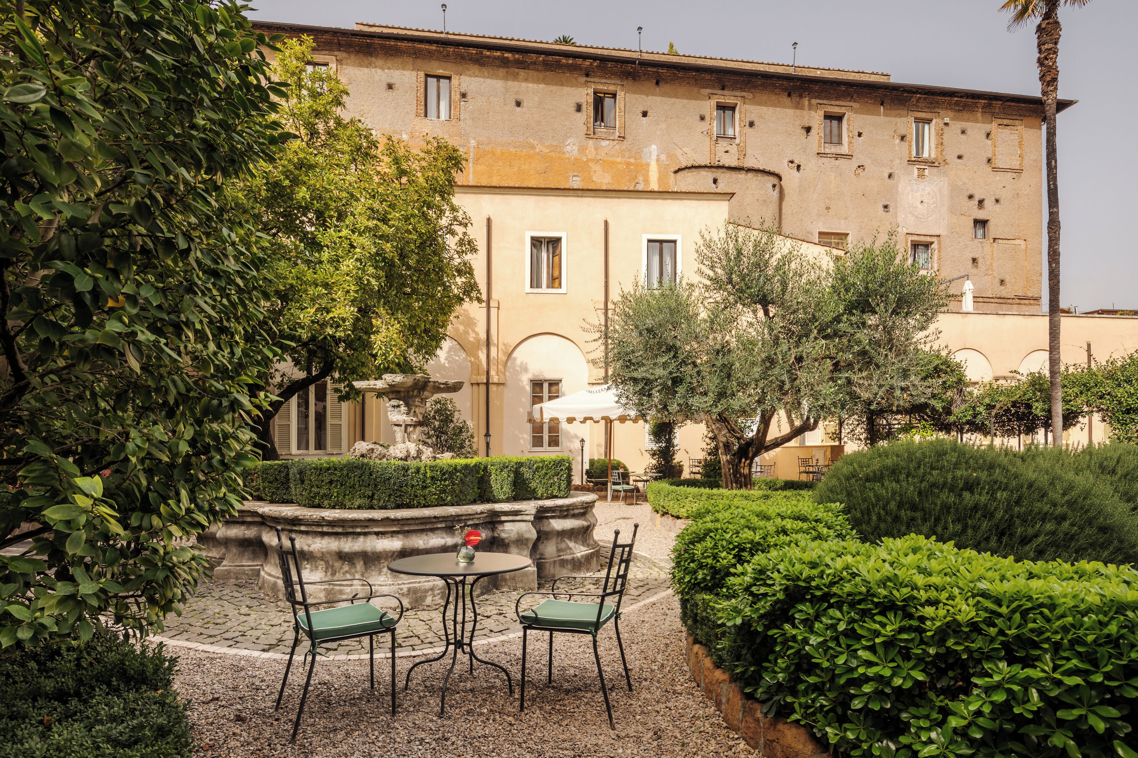 A courtyard with a fountain, two tables with chairs, and a building with multiple windows.