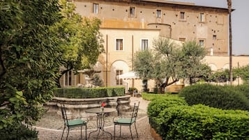 A courtyard with a fountain, two tables with chairs, and a building with multiple windows.