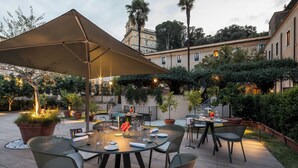 An outdoor patio with round tables and chairs, a large umbrella, and potted plants. - Donna Camilla Savelli – VRetreats (Rome)