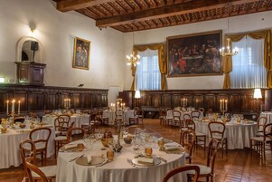 A formal dining room with round tables, chairs, and candlelit chandeliers.