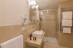 A modern bathroom with a large sink, a mirror with lights, a shower, and a towel rack.