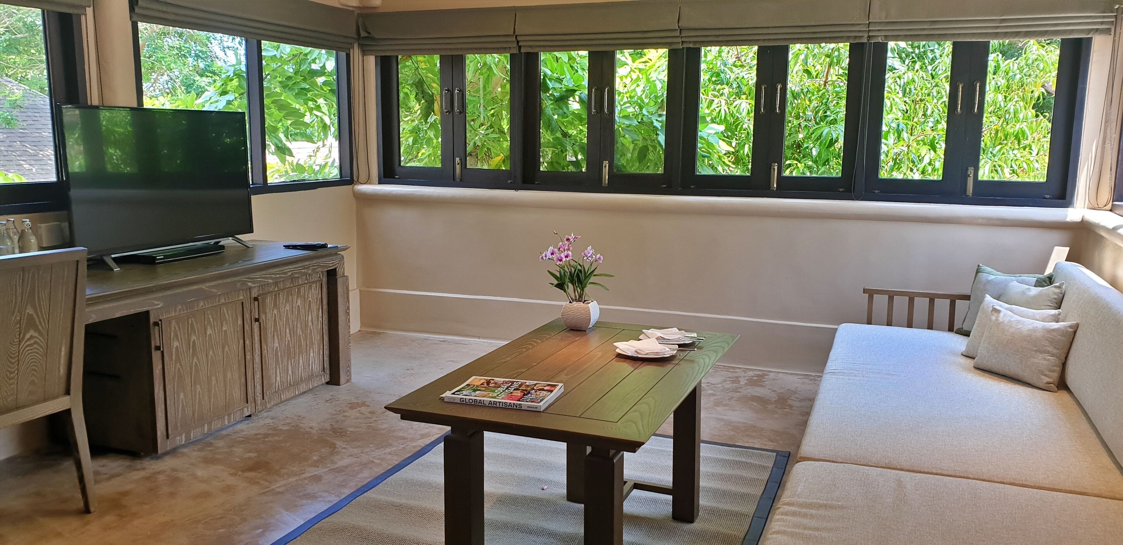 Un salon avec un téléviseur, un meuble en bois, un canapé et une table sur laquelle se trouvent un magazine et des fleurs.